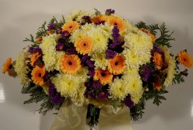 ovales Trauergesteck in gelb/lila mit Gerbera, Chrysanthemen und dekorativem Beiwerk.